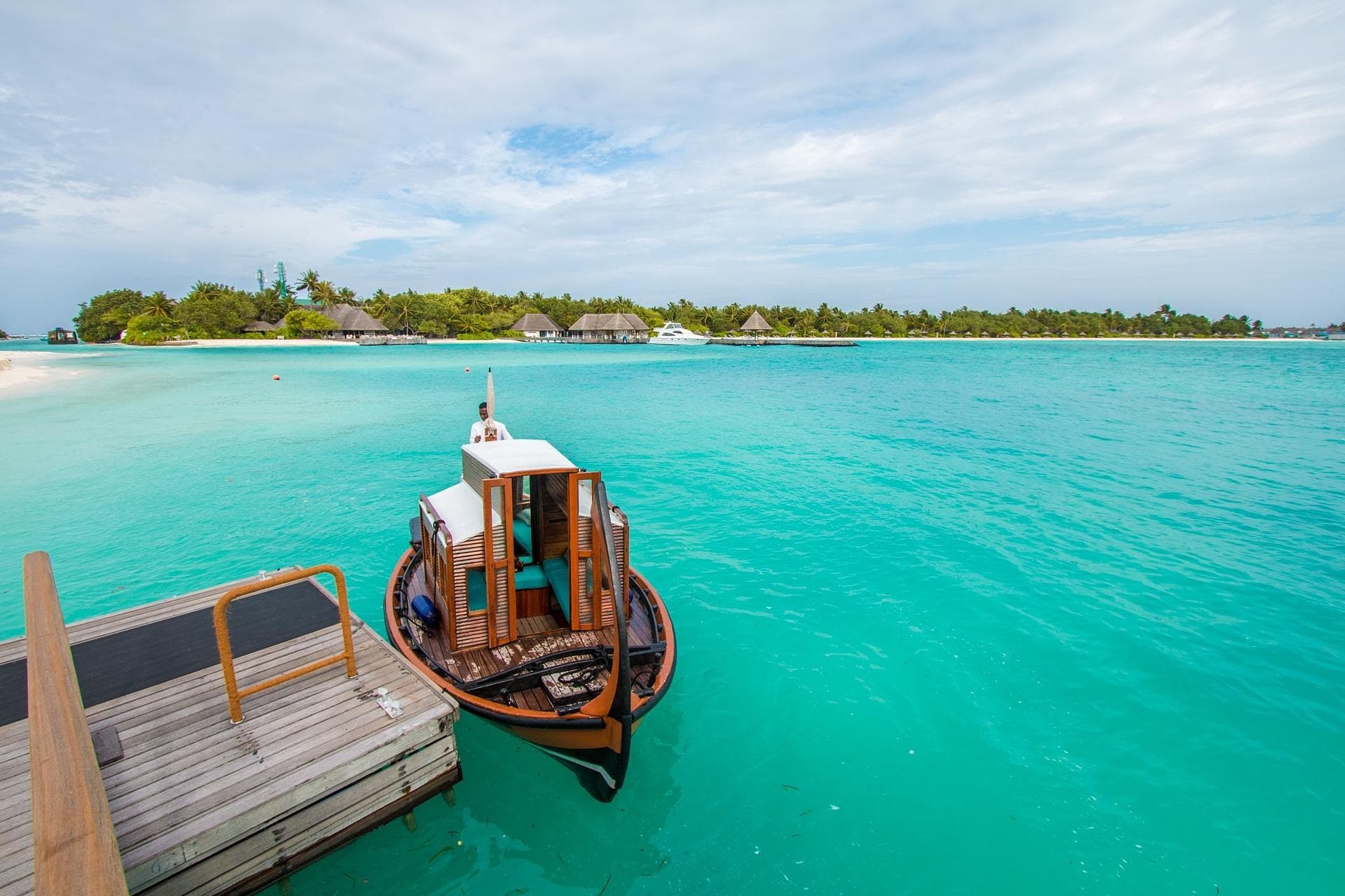 Traditional Maldivian dhoni boat at a resort dock with turquoise lagoon